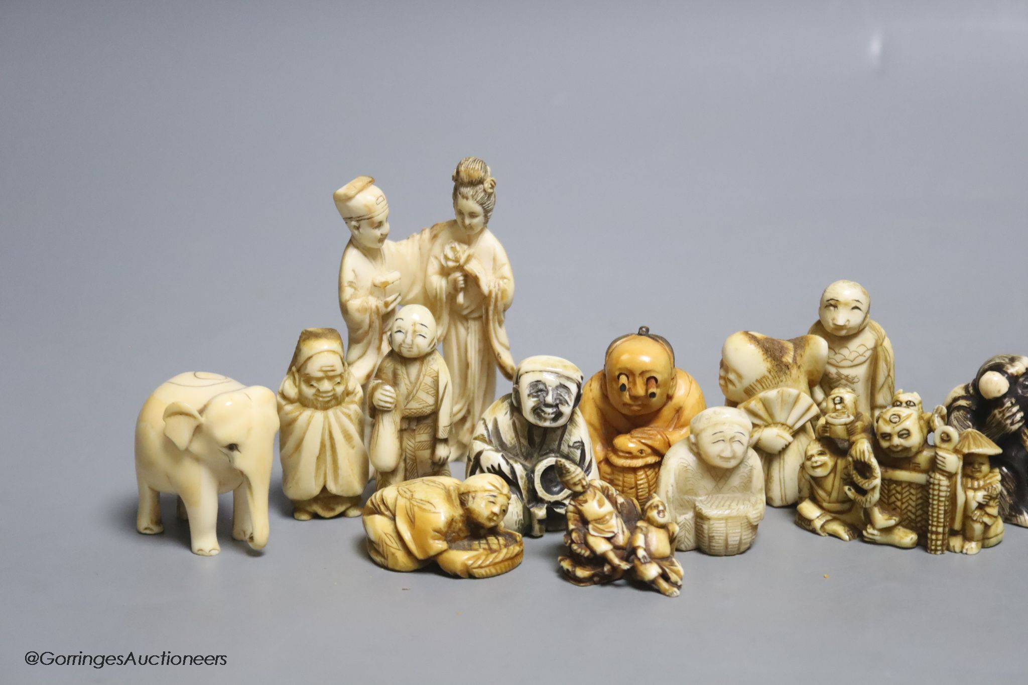 Fourteen Japanese ivory netsuke, a Chinese ivory group and elephant figure, all early 20th century